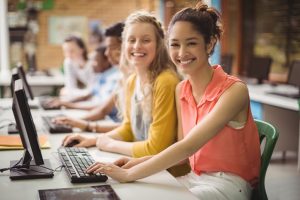 16 Year Old Girls Sitting At A Computer Desk Smiling for the Camera